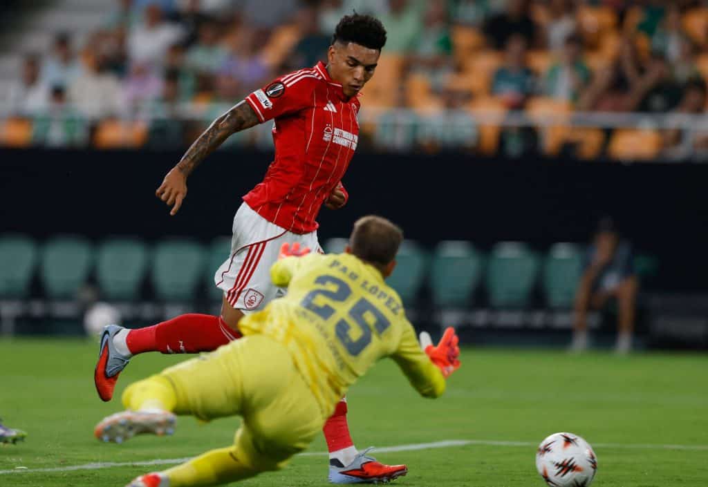 Vibrant soccer match action featuring a player in red jersey dribbling past a goalkeeper in yellow uniform during an intense game. Fans and stadium background add excitement.