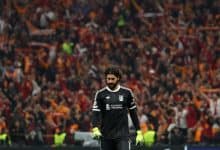 Excited soccer goalkeeper in black uniform with crowd in stadium background during match at ZareSport.et.