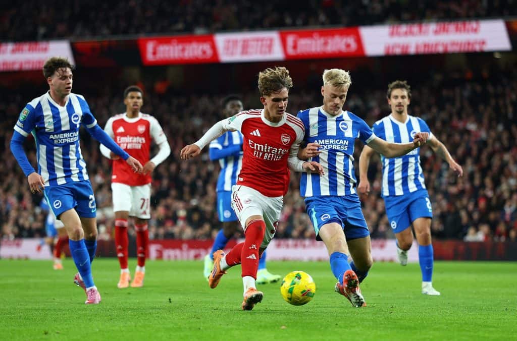 Bright soccer match featuring players from Arsenal and Brighton & Hove Albion competing for possession of the ball during a professional English Premier League game.