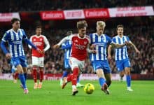 Bright soccer match featuring players from Arsenal and Brighton & Hove Albion competing for possession of the ball during a professional English Premier League game.