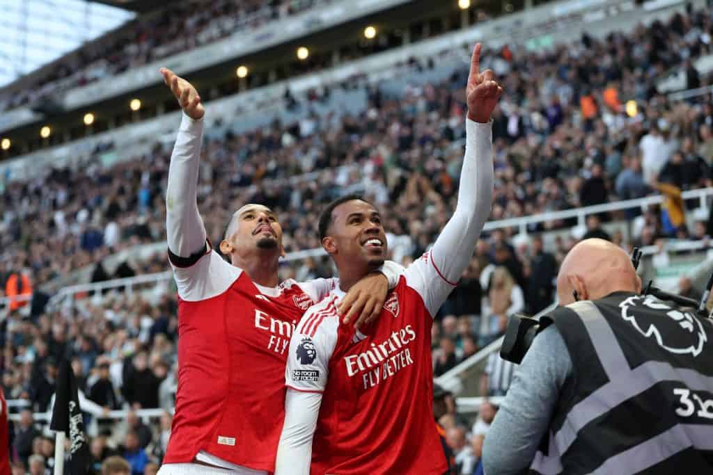 Bright professional soccer players celebrating victory at a stadium during a match, wearing red and white jerseys, with a lively crowd in the background, capturing the excitement of sports and team success.