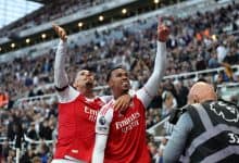 Bright professional soccer players celebrating victory at a stadium during a match, wearing red and white jerseys, with a lively crowd in the background, capturing the excitement of sports and team success.