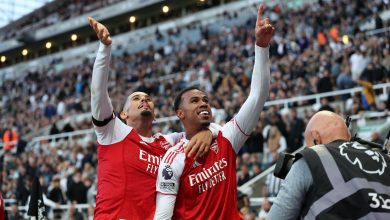 Bright professional soccer players celebrating victory at a stadium during a match, wearing red and white jerseys, with a lively crowd in the background, capturing the excitement of sports and team success.