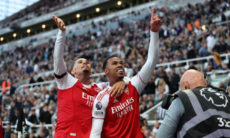 Bright professional soccer players celebrating victory at a stadium during a match, wearing red and white jerseys, with a lively crowd in the background, capturing the excitement of sports and team success.