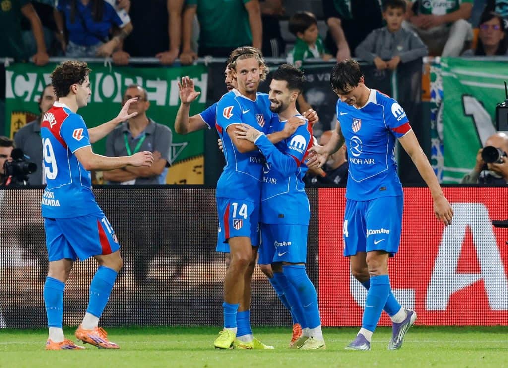 Vibrant soccer players celebrating a goal during an athletic match on the field, showcasing teamwork and sportsmanship, with a lively crowd in the background.