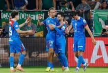 Vibrant soccer players celebrating a goal during an athletic match on the field, showcasing teamwork and sportsmanship, with a lively crowd in the background.