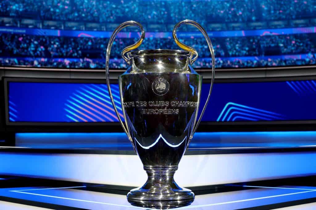 Shiny UEFA Champions League trophy on a presentation platform with a vibrant stadium background, celebrating European football success, iconic sports event trophy, ZareSport.et sports news.