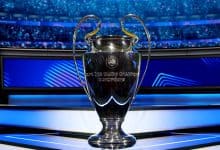 Shiny UEFA Champions League trophy on a presentation platform with a vibrant stadium background, celebrating European football success, iconic sports event trophy, ZareSport.et sports news.