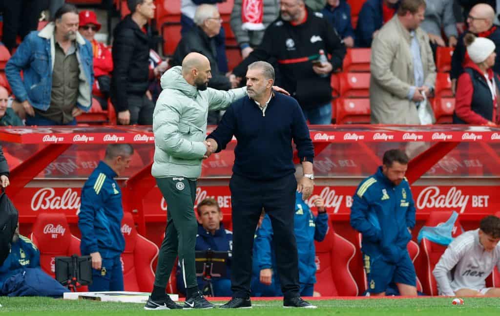 Handshake between two soccer coaches on the sideline of a football match, with team staff and spectators in the background.