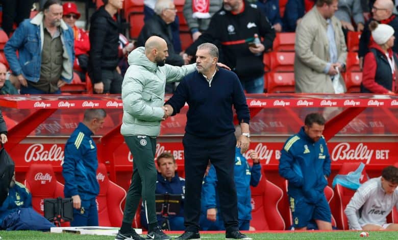 Handshake between two soccer coaches on the sideline of a football match, with team staff and spectators in the background.