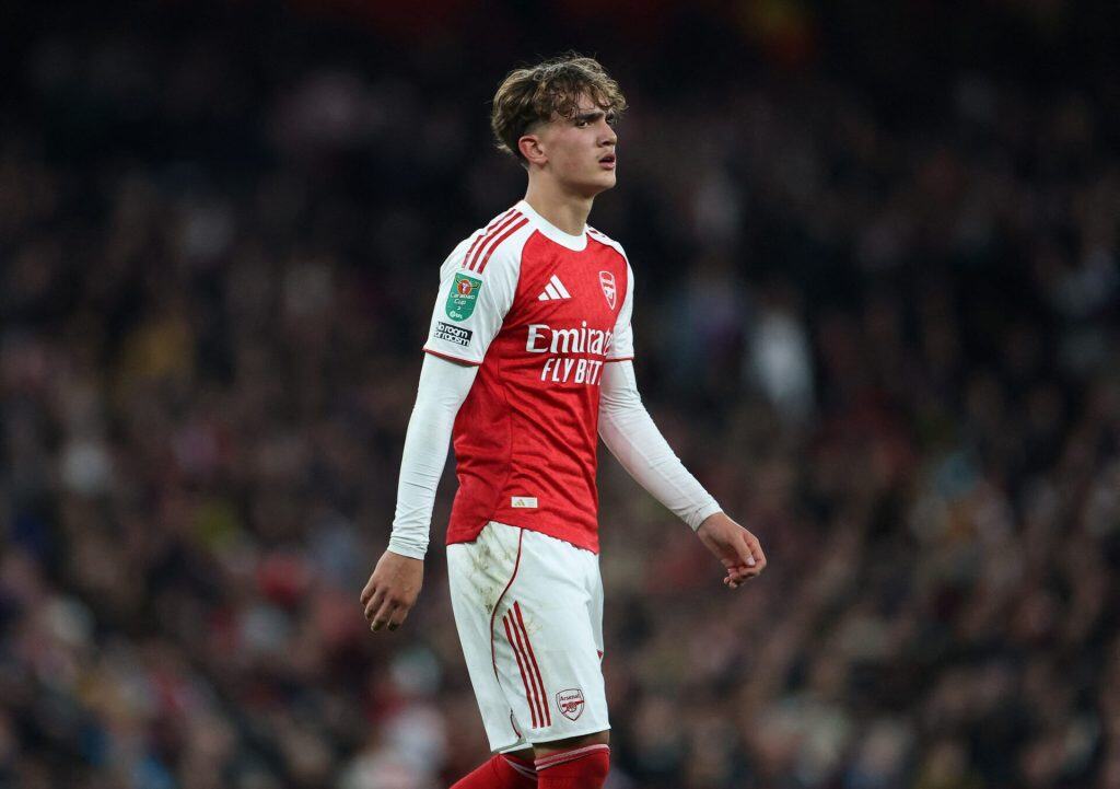 Young male soccer player in Arsenal jersey during match, stadium background, focused expression.