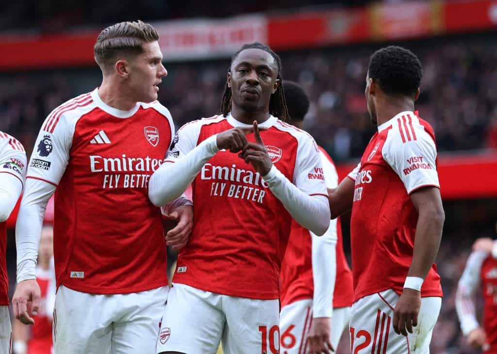 Excited Arsenal football players celebrating on the field during a match, wearing red and white jerseys with sponsor logos, showcasing team spirit and camaraderie.