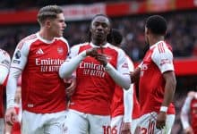 Excited Arsenal football players celebrating on the field during a match, wearing red and white jerseys with sponsor logos, showcasing team spirit and camaraderie.