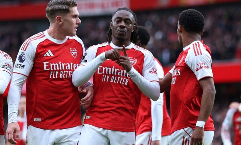 Excited Arsenal football players celebrating on the field during a match, wearing red and white jerseys with sponsor logos, showcasing team spirit and camaraderie.