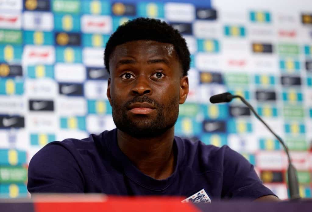 Palace Face Guehi Dilemma: Sell Now or Lose Him for Free? African male athlete at sports press conference, wearing team jersey, with sponsor logos in background.