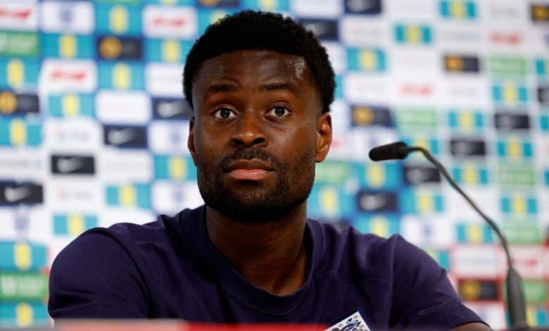 Palace Face Guehi Dilemma: Sell Now or Lose Him for Free? African male athlete at sports press conference, wearing team jersey, with sponsor logos in background.