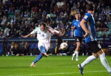 Dynamic soccer match featuring Italian and Finnish players competing for ball possession during a night game. Fans fill the stadium in the background.