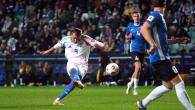 Dynamic soccer match featuring Italian and Finnish players competing for ball possession during a night game. Fans fill the stadium in the background.