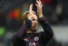 Energetic football player clapping during match, wearing Bayern Munich jersey, celebrating teamwork and sportsmanship on the field.