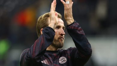 Energetic football player clapping during match, wearing Bayern Munich jersey, celebrating teamwork and sportsmanship on the field.