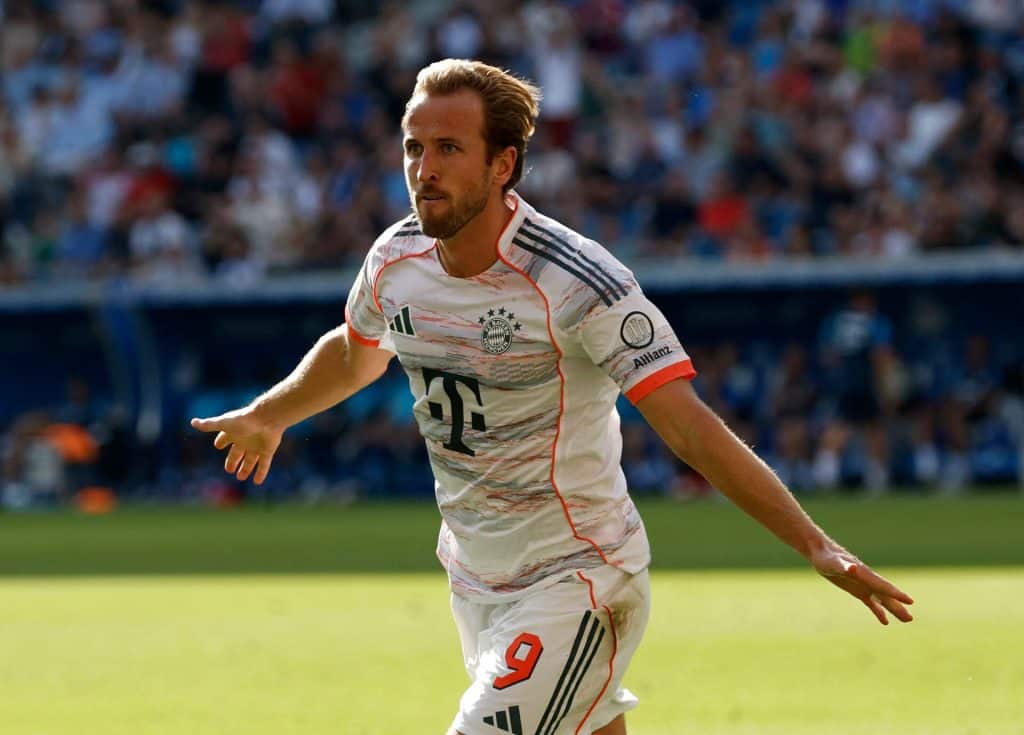 Harry Kane’s Bayern Love Story: Why He Might Never Come Back Dynamic soccer player in Bayern Munich jersey celebrating a goal on the field during a match, with a lively crowd in the background, showcasing athleticism and passion for sports.