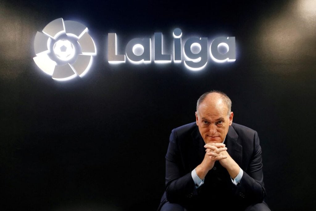 Professional man in formal suit sitting in front of La Liga logo at Zaresport.et sports website, promoting football, sports management, and La Liga partnerships.