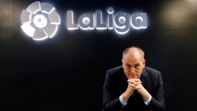 Professional man in formal suit sitting in front of La Liga logo at Zaresport.et sports website, promoting football, sports management, and La Liga partnerships.