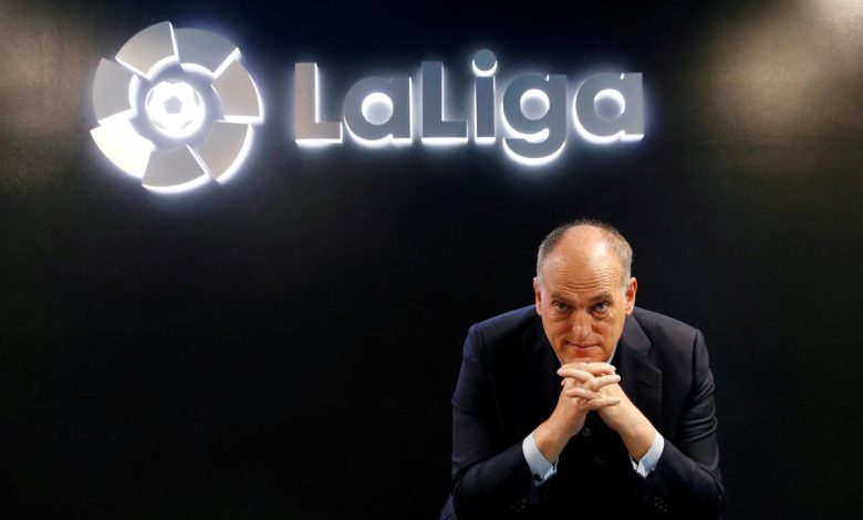 Professional man in formal suit sitting in front of La Liga logo at Zaresport.et sports website, promoting football, sports management, and La Liga partnerships.