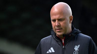 Bald football coach in black sports jacket with Liverpool FC logo, outdoors, focused expression, team management, sports training, leadership, athletic apparel, professional coach, sports apparel, coaching staff, sports performance, soccer training, team strategy, football training, sport coaching, athlete development, soccer team, sports leadership, athletic coaching, sports management, football club, sports professionalism, team sports, coaching expertise, athlete mentoring, soccer tactics, sports motivation, team unity, football tactics, sports discipline, player development, athletic success, sports passion, coaching career, sports excellence, competitive sports, soccer game, sports background, athletic discipline.