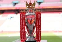 Victory League trophy with red ribbons, golden lions, and crown detail, awarded for Premier League achievements, displayed in a football stadium.