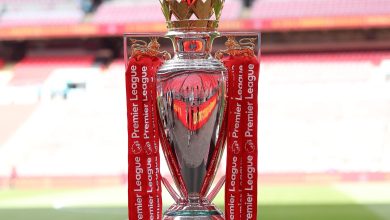 Victory League trophy with red ribbons, golden lions, and crown detail, awarded for Premier League achievements, displayed in a football stadium.