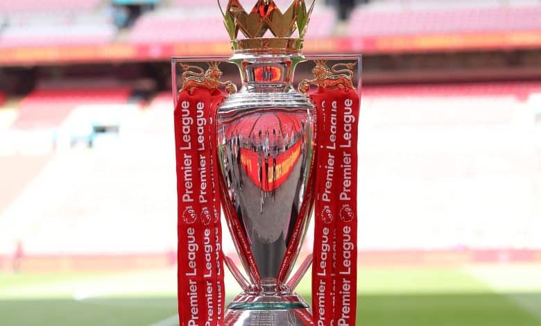 Victory League trophy with red ribbons, golden lions, and crown detail, awarded for Premier League achievements, displayed in a football stadium.