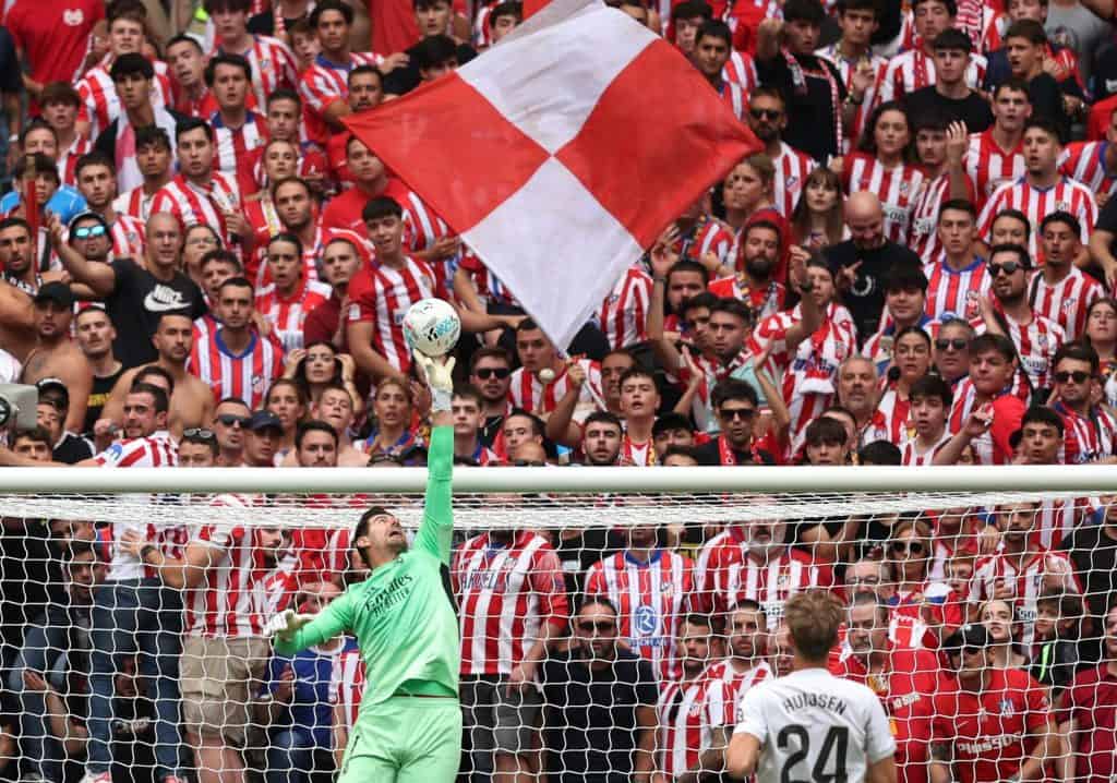 Fans cheering at Atletico Madrid football match, passionate supporters in red and white striped jerseys, intense stadium atmosphere, and team spirit.