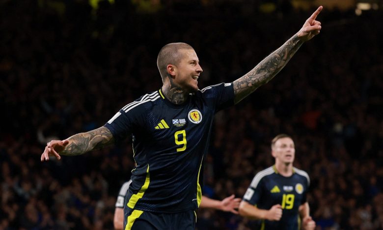 European Night of Goals: Denmark Dominate, Scotland Rise, Faroe Islands Shock Everyone Vibrant image of a football player celebrating a goal during a match, wearing a dark blue jersey with yellow accents and the number 9, with arms raised and tattoos visible, stadium filled with fans in the background.