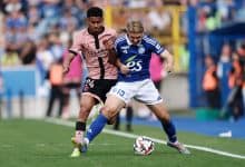Young soccer players competing in a match, one in a pink jersey and the other in a blue jersey, battling for control of the ball on a vibrant green field.