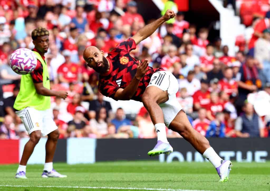 Dynamic soccer player in Manchester United kit making an acrobatic save during match with fans in the background, showcasing athleticism and team spirit, vibrant sports action photography.