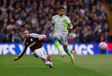 Dynamic soccer players competing during match, one sliding while the other jumps for the ball, on a professional football field, emphasizing sports competition, athleticism, and teamwork.