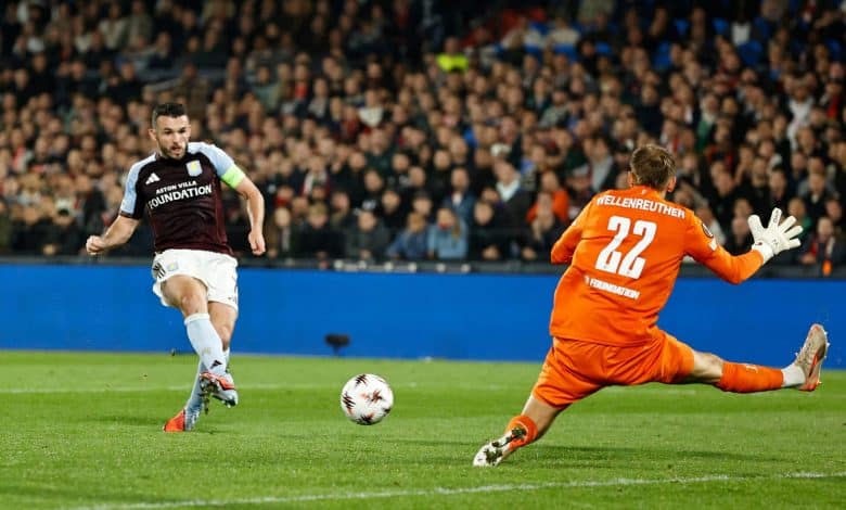 Underdogs Steal the Show on a Wild Europa League Night Aston Villa player in a black and blue kit and goalkeeper in orange uniform during a football match with a crowded stadium in the background.