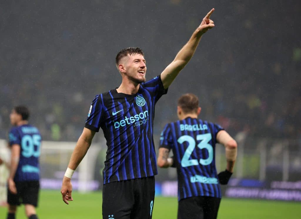 Dynamic football player celebrating a goal during a match, wearing Inter Milan jersey, raising his arm in triumph, team members in the background, rainy atmosphere, showcasing sports passion.