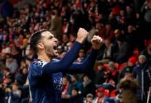 Vibrant football player celebrating in packed stadium, showing victory with arms raised, wearing team kit, in front of energetic crowd.