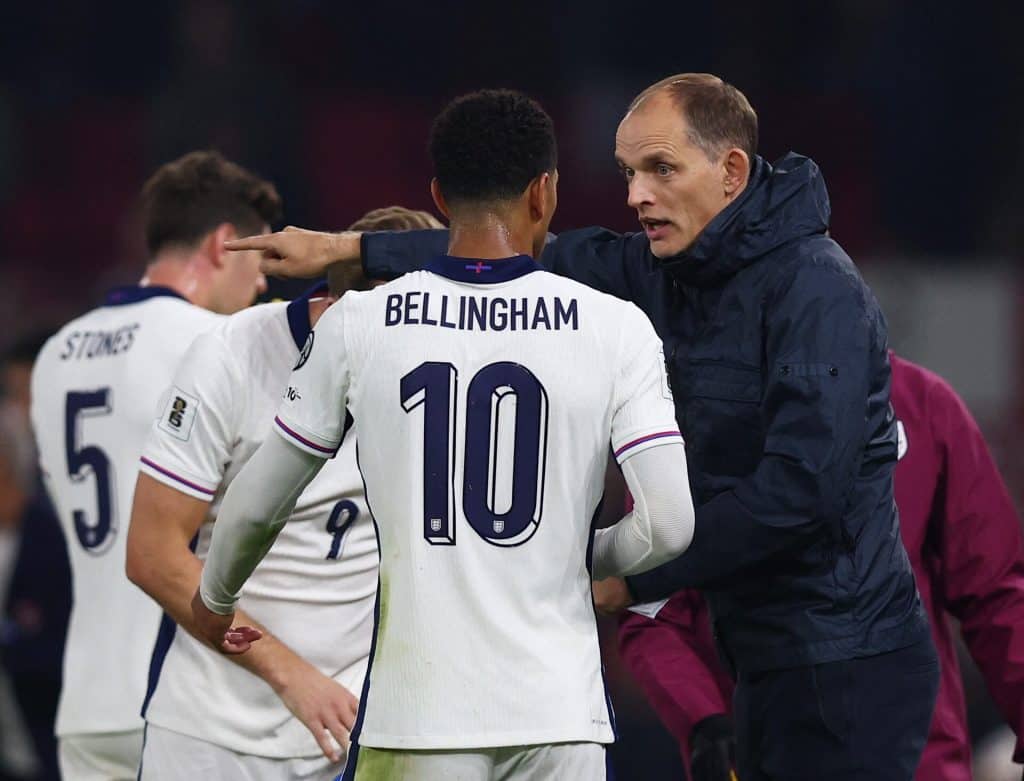 Striker Harry Bellingham wearing England national team jersey during match, talking to coach in intense moment, with team players in background, emphasizing soccer, teamwork, and sports coaching themes.