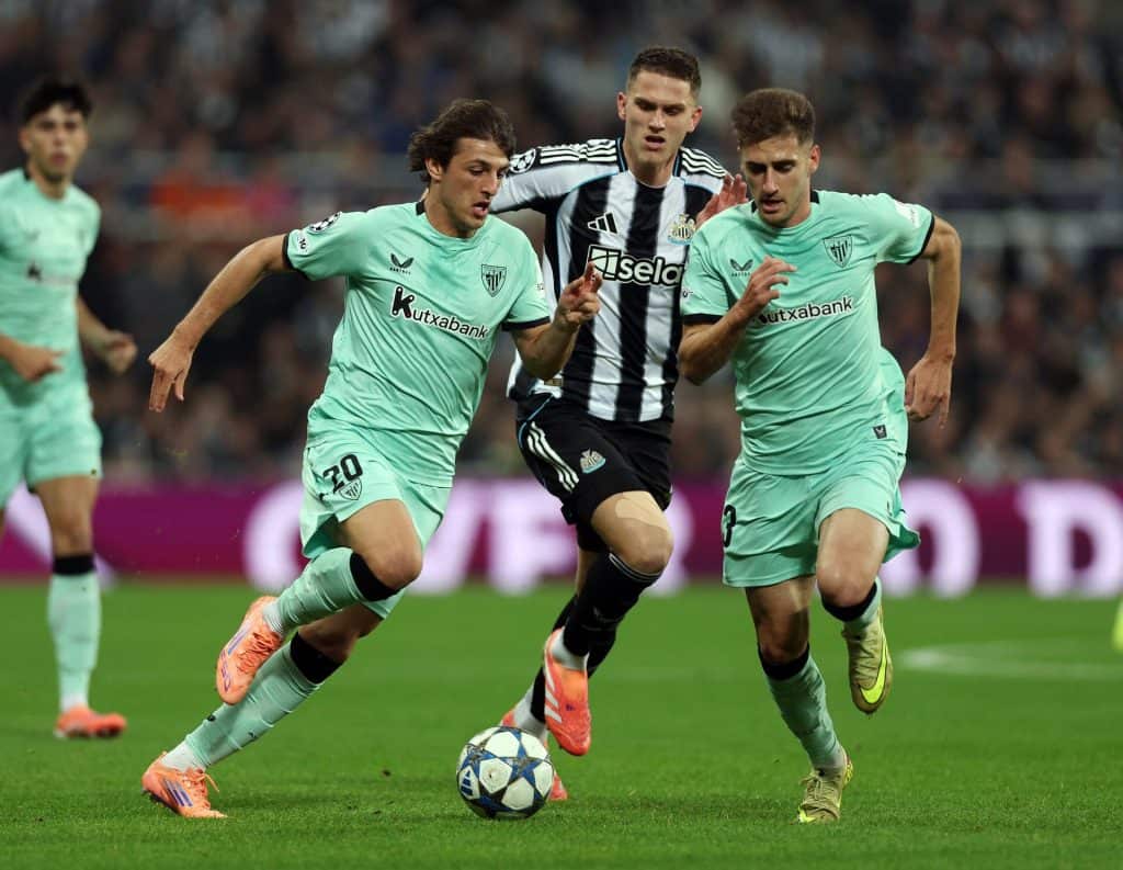 Dynamic soccer players battling for ball control during a match, wearing team jerseys, in a full stadium setting.