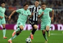 Dynamic soccer players battling for ball control during a match, wearing team jerseys, in a full stadium setting.