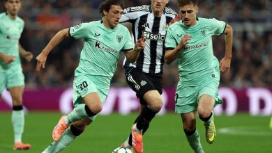 Dynamic soccer players battling for ball control during a match, wearing team jerseys, in a full stadium setting.
