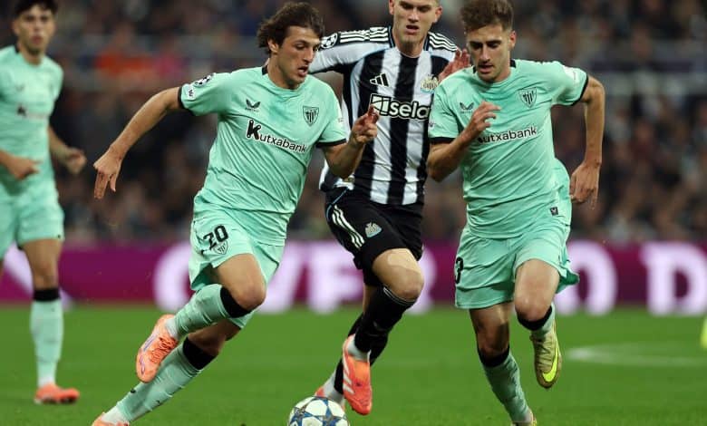 Dynamic soccer players battling for ball control during a match, wearing team jerseys, in a full stadium setting.