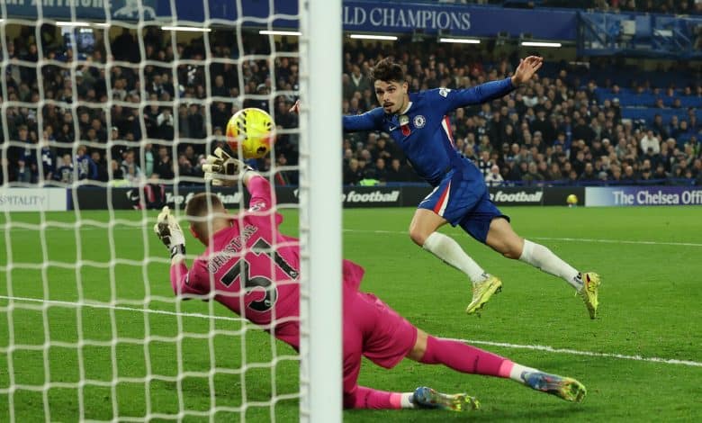 1. Soccer player in Chelsea kit scoring a goal past goalkeeper in pink goalkeeper uniform during match at Stamford Bridge stadium.