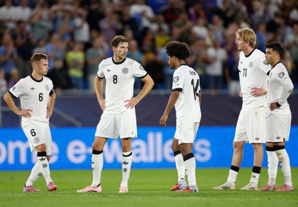 Young soccer players in white jerseys on the field during a match, team strategizing and discussing game tactics in front of a crowd.