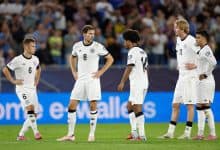 Young soccer players in white jerseys on the field during a match, team strategizing and discussing game tactics in front of a crowd.