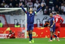 Ethiopian soccer player celebrating a goal on the field during a match, wearing a blue jersey with the number 4, with teammates and opponents visible in the background.