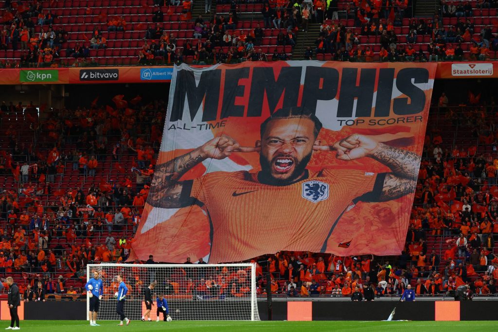 Memphis Depay football fan banner at stadium, orange jersey supporter cheering, soccer match, sports event, fan enthusiasm, Memphis all-time top scorer, stadium crowd, Netherlands national player, passionate football crowd, Zaresport.et SEO imagery.